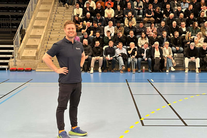 En Blostrupmoen instruktør står forran 200 mennesker og holder kurs. Kurset finner sted i en idrettshall og kursdeltagere sitter på tribunen.