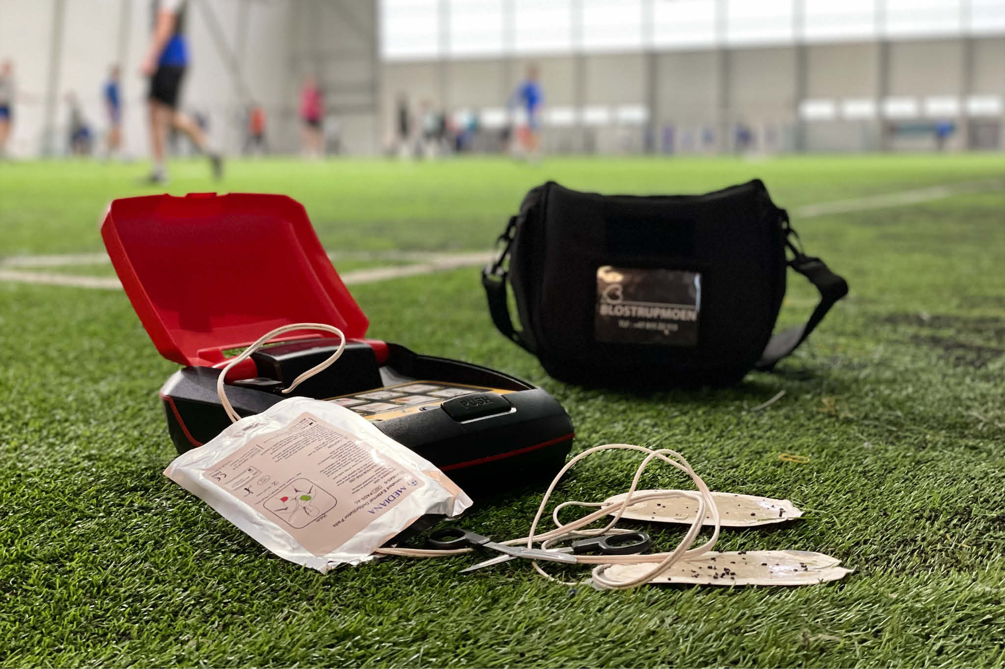 En hjertestarter som er brukt i en hendelse. Elektrodene viser at den er full ab kroppshår og skitt. Den ligger på en kunstgressbane der den ble brukt.