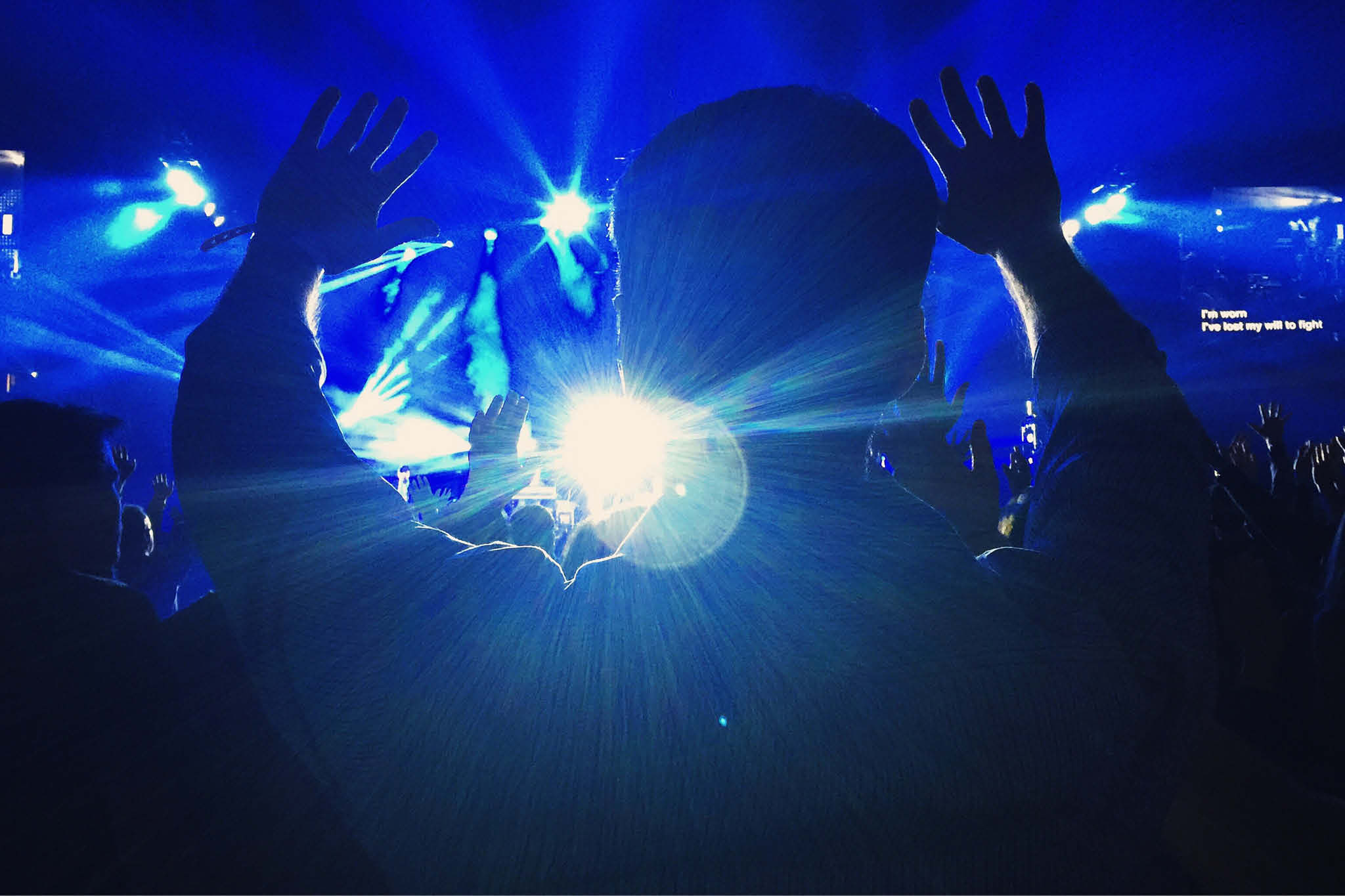 Mange mennesker står forran en scene og fester til musikerne som står på scenen. Det er discolys.