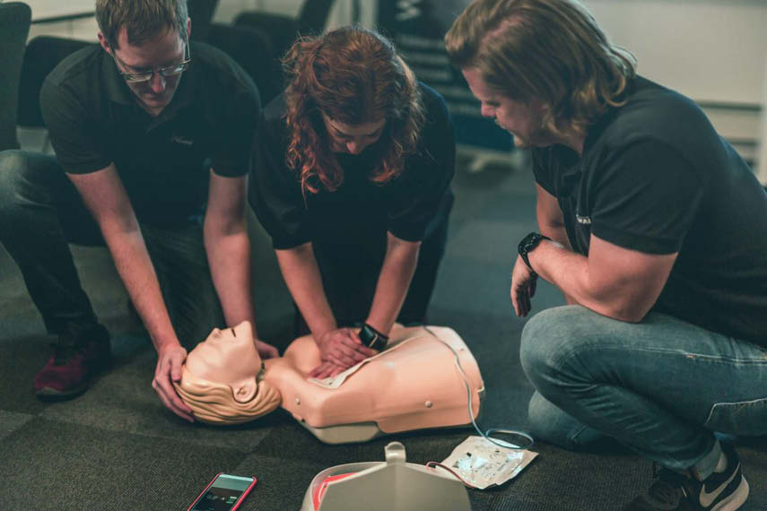 To kursdeltagere utfører HLR på en dukke og en instruktør forteller hvordan de skal gjøre det