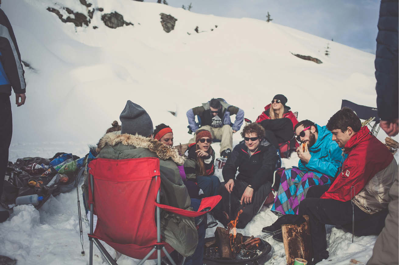 En gjeng unge voksne sitter rundt et bål i påskefjellet og griller pølser på tur.